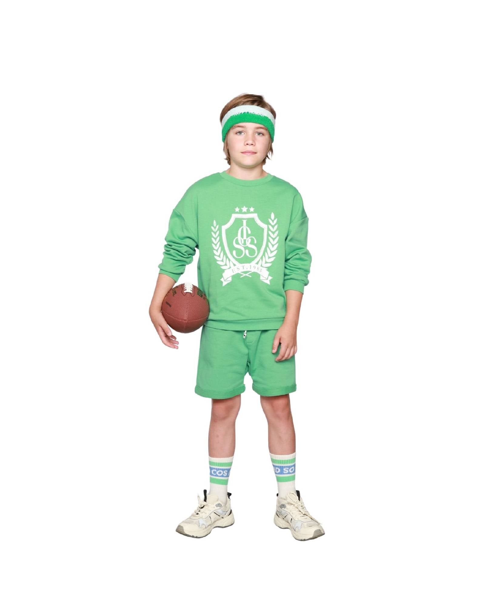 Boy model wearing the Happy Human Headband with the Country Club Sweater and Jog Shorts in Spruce Green, with CISS socks.