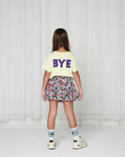 Girl model wearing the T-Shirt in the color Lime Cream with caption BYE in capital in dark purple centered on the backside.