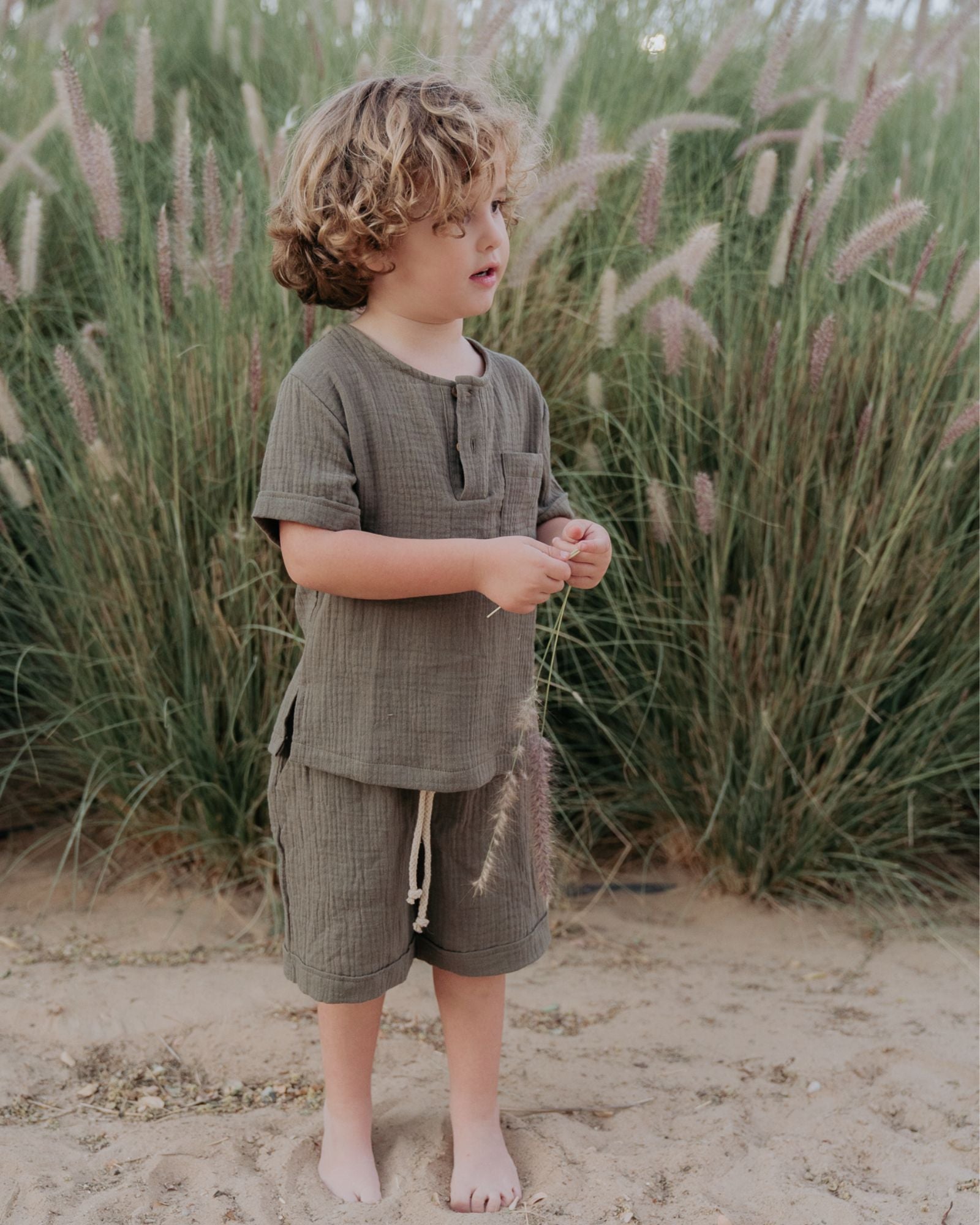 Boy model wearing the Charlie Shirt in Soft Khaki Green Muslin Cotton, matching the Julian Shorts in Soft Khaki Green Muslin Cotton.