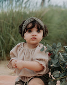 Baby girl wearing an outfit by Les Vedettes in high quality Muslin Cotton. The Alexa Top in Beige with the Chlochlo bloomers in Khaki Embroidery and the Twisted Headband in Soft Khaki Green.